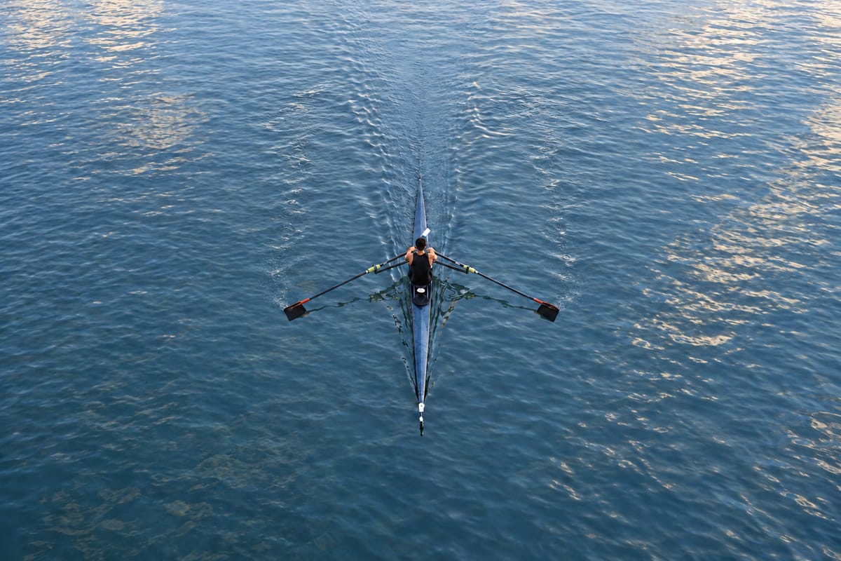 A single rowing boat on still, blue water, seen from high above.