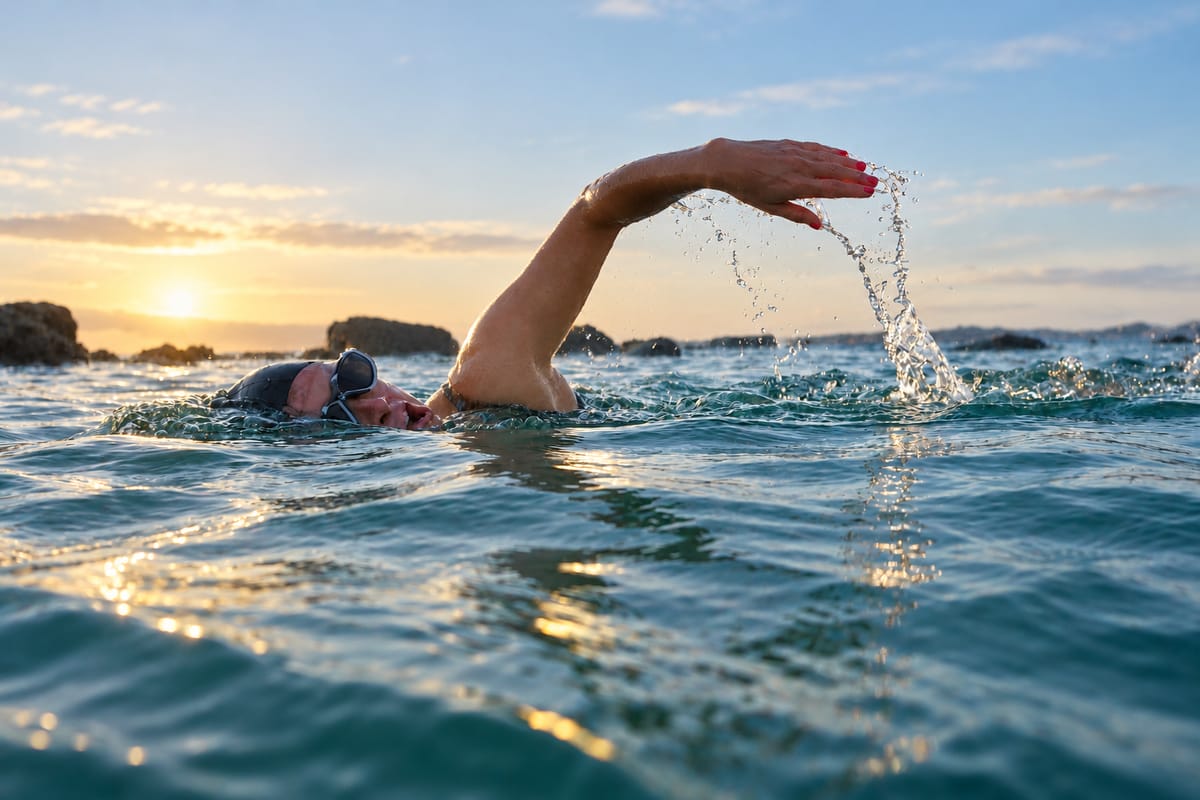 A swimmer does front crawl in the sea at sunrise, water falling from her hand.